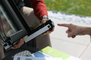 Close-up of two people examining an aluminum window frame outdoors.