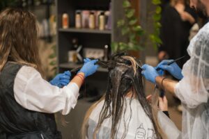 Professional stylists dyeing a woman's hair in a modern salon setting, showcasing teamwork and expertise.