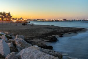 A peaceful beach view with city lights at dusk, capturing the serene waterfront and urban skyline.