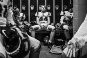 Intense black and white photo captures high school football players in a locker room pre-game.